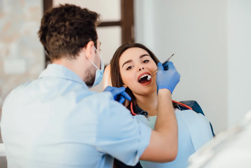 Professional teeth cleaning by dentist with cotton on young female patient in dental office